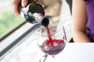 close-up of a bottle of red wine being poured into a wine glass by a server